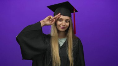 Mezuniyet üniformalı genç bir kadın, izole edilmiş mor bir geçmişe karşı güvenle poz veriyor, bu da eğitimde başarı ve başarı anlamına geliyor..