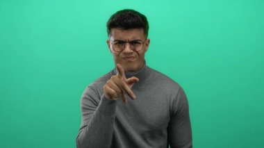 Genç adam canlı yeşil bir arka planda, gözlükleriyle güven içinde el kol hareketi yaparak, izole edilmiş, modern ve şık bir portre çiziyor..