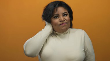 Turuncu arka plandaki kadın kendinden emin değil, gözleri kapalı ve elleri boynunda, kafa karışıklığı ve belirsizliği açıkça ifade ediyor..