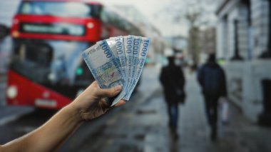 Açık hava otobüs durağında arkasında bulanık bir otobüs ve yayalar olan Macar banknotları tutan adam dinamik bir şehir manzarası yaratıyor..