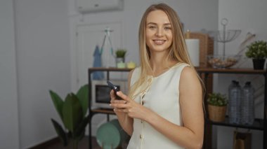 Çağdaş ofiste gülümseyen bir kadın, elinde bitkilerle sarışın, beyaz, çekici bir kadın, kapalı alanda çalışıyor..