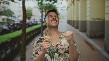 Genç adam heyecan içinde bir şehir caddesinde dondurma yiyor, şehir ortamında mutluluk ve macerayı somutlaştırıyor..