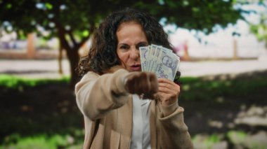 Orta yaşlı bir kadın parkta heyecanla Romanya banknotlarını tutuyor. Açık havada mali başarıya işaret ediyor..