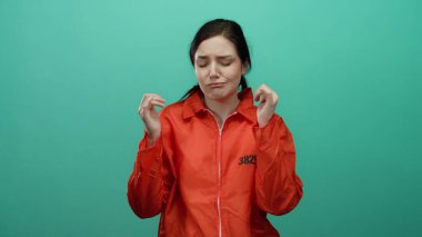 Turuncu hapishane tulumu giyen kadın canlı yeşil bir arkaplan karşısında neşeli bir şekilde dans ediyor, esmer saçı ve rahat tavırlarıyla neşe ve özgürlüğü ifade ediyor..