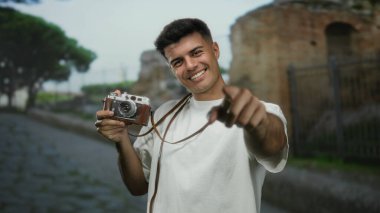 Şehrin dışındaki bir sokakta eski bir kamerayla gülümseyen genç bir adam canlı ve çekici bir hava yayıyor..