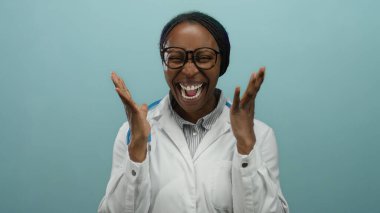 Steteskoplu beyaz önlüklü gülümseyen Afrikalı kadın arka planda sevinçle kutlama yapıyor.