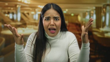 Restoran ortamında hayal kırıklığını ifade eden bir kadın, kapalı bir kahve dükkanında jestlerle duygularını sergiliyor..