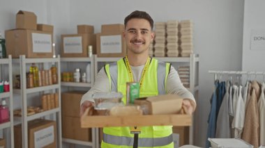 Yansıtıcı yelek giyen genç adam kapalı bir hayır kurumunda gönüllü olarak yemek tepsisi taşıyor..