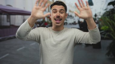 Genç İspanyol asıllı bir adam şehir sokaklarında neşeli hareketler yapıyor, çevresini çevreleyen hareketli şehir hayatı, neşeli bir ortamda neşe ve doğallığı ifade ediyor..