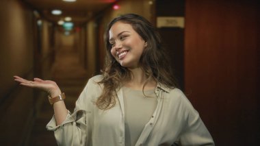 Gülümseyen kadın, aydınlık modern otel binasında kol saatini göstererek el ele uzanır; neşe içinde karşılanır.