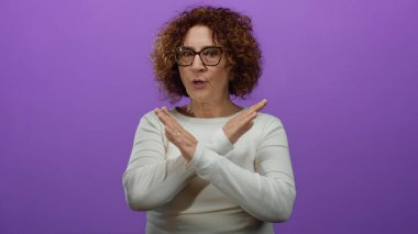 Orta yaşlı İspanyol bir kadın, beyaz bir bluzla, izole edilmiş mor bir arka plana karşı duruyor..