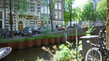 Bisikletler, yeşillik ve park halindeki arabalarla Amsterdam Kanalı 'nın bulanık görüntüsü. Odaklanamayan, canlı Bokeh etkisine sahip kentsel Hollanda atmosferini gözler önüne seriyor..