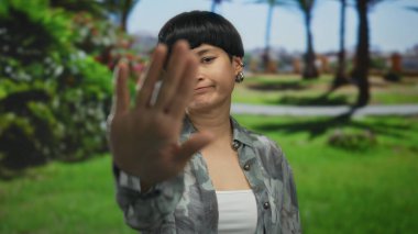 Genç Çinli bir kadın, açık hava parkı ortamında, parlak, berrak gökyüzünün altında yemyeşil bir yeşil ile çevrili bir yerde el hareketi yapıyor..