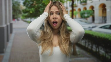 Sarışın kadın, park halindeki arabaları ve çitleri olan hareketli şehir kaldırımında avuçlarını açar. Şaşırtıcı şaşkınlık şokuna tutulur..