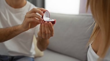 Erkek, evde kadına nişan yüzüğüyle evlenme teklif eder. Ev ortamında sevgi ve ilişki gösterir. Oturma odasında çiftle romantik bir anı ön plana çıkarır..