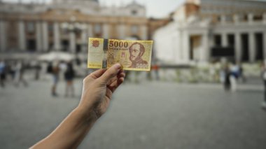 Vatikan 'ın kalabalık sahnesinde el ele tutuşan Macar banknotları. St. Peter Meydanı' nda yürüyen turistler, kültürü karıştırıyor ve Avrupa 'nın ikonik mimarisi ile seyahat ediyor..