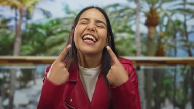 Güneşli bir parkta gülümseyen bir kadın açık havada yemyeşil ağaçlarla çevrili kırmızı bir ceket giyiyor. Mutluluğu ve gençlik enerjisini somutlaştırıyor.