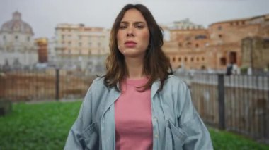 Latin kadın, Roma harabeleri yakınlarındaki gürültü nedeniyle kulaklarını kapatıyor. İfadesi, tarihi şehir zeminine karşı rahatsızlığını gösteriyor ve kentsel zorlukları vurguluyor..