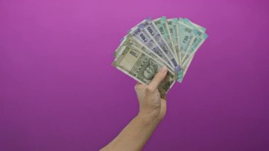 Kafkasyalı bir adam, canlı pembe bir duvara karşı elinde Hint rupisi banknotları tutuyor, izole bir ortamda para ve finansal konseptler sergiliyor..
