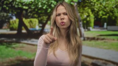 Kadın işaret parmağı ile şehir parkında işaret parmağı ileri odaklanmış bakış ve görünür el hareketi; öfke azarlama uyarısı.