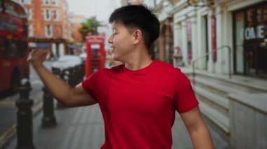 Kırmızı tişörtlü genç Çinli adam hareketli ve ikonik mimari ile dolu canlı bir şehir caddesinde kaslarını kasıyor..