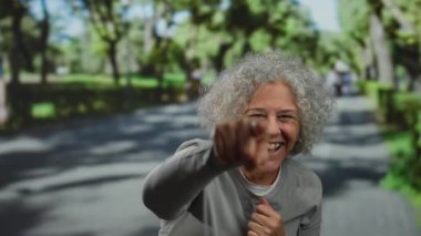 Gri saçlı yaşlı bir kadın güneşli bir açık hava parkında neşeyle gülerek mutluluk ve tasasız anları gösteren sıcak ve canlı bir ortam sağlıyor..