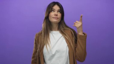 İzole edilmiş mor bir arkaplan üzerine düşünceli bir yüz ifadesiyle yukarı bakan kadın, yaratıcı ya da fikir temalı bir konsepti işaret ediyor.