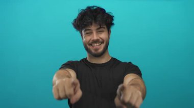 Sakallı, gülümseyen ve mavi arka planda kameraya bakan genç bir İspanyol, davetkar bir ortam yaratıyor..