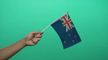 Ulusal gurur ve vatanseverliği temsil eden, yeşil arka planda el ele tutuşan yeni Zelanda bayrağı.