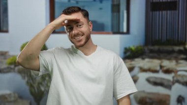 Şehir sokaklarında sakallı ve kısa saçlı gülümseyen genç bir adam modern bir arka plana sahip açık bir şehir ortamında günlük beyaz bir gömlek giyiyor..