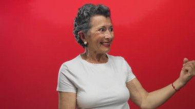 Gri saçlı, gülümseyen ve elleri kıpkırmızı arka planda hareket eden, neşeli ve neşeli bir sahnede neşe ve nişanı ifade eden son sınıf öğrencisi kadın..