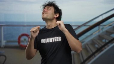 Gönüllü tişört giyen İspanyol bir adam arka planda okyanus olan bir yolcu gemisinin güvertesinde neşeyle dans ediyor. Mutluluk ve coşku yayıyor..