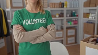 Yeşil tişörtlü bir kadın bir depoyu işaret ediyor. Genç bir sarışın gönüllü yardım etkinliği için kollarını kavuşturup gülümsüyor..