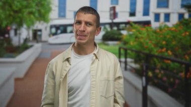 Şehir caddesinde duygularını ifade eden bir adam yeşil yapraklı ve arka planda modern binalar açık şehir manzarasını gösteriyor..