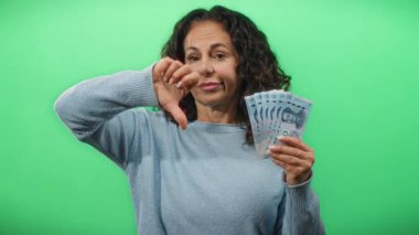 Orta yaşlı bir kadın yeşil bir duvara karşı Çin Yuan banknotları tutuyor. Bu da paradan memnun olmadığını ya da memnun olmadığını gösteriyor..