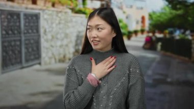 Şehir caddesinde açık havada, göğsünde gri bir kazak olan bir kadın şehir ortamında şaşkınlığını ifade ediyor.