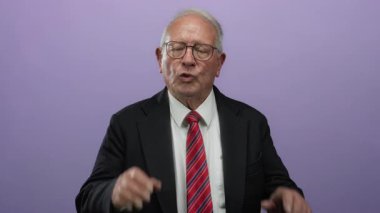 Takım elbiseli kıdemli bir adam, izole edilmiş mor arka plana karşı sakin bir şekilde el kol hareketi yapar..