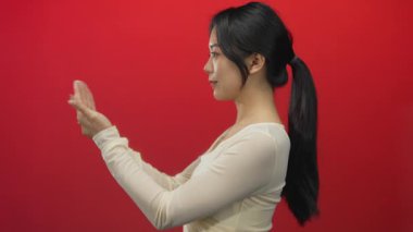 Çinli bir kadın, elleri açık, canlı kırmızı bir arka plana karşı duruyor, kendine güven ve pozitiflik yayıyor, kültürel zarafeti ve modern modayı özgüvenli bir zarafetle vurguluyor..