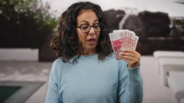 Bir şehir caddesinde elinde İzlanda Krona banknotları tutan orta yaşlı bir kadın açık şehir ortamında ekonomi ve finans kavramları sergiliyor..