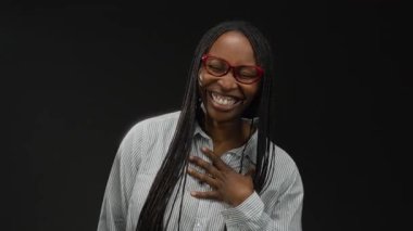 Bana bir jestle gülümseyen bir kadın, karanlık bir arka planda izole edilmiş, doğal güzelliğini ve özgüvenini sergiliyor..