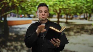 Güneşli bir parkta, ağaçlarla çevrili siyah bir cübbe ve haç içinde İncil okuyan İspanyol bir rahip..
