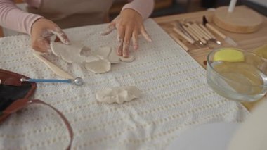 Kadın elleri, çömlek atölyesindeki su kasesi ve kil aletlerle ahşap bir masada kilden kalp formları oluşturan eller; yaratıcılık odaklı..