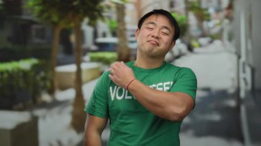 Yeşil tişörtlü genç adam şehir sokağında güvenle duruyor.