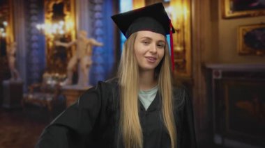 Mezuniyet elbisesi giymiş genç bir kadın zarif bir müzede kendine güvenerek poz veriyor. Sanat ve kültür özetlerini sergiliyor..