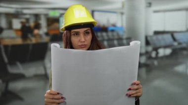 Havaalanı terminalinin planlarını inceleyen kadın mühendis, mimari unsurların olduğu kapalı bir ortamda dikkatini çekiyor..