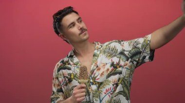 Çiçekli tişörtlü genç adam selfie çekiyor ve canlı kırmızı bir arka planda dondurma tutuyor neşeli tatil havası sergiliyor..