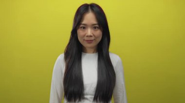 Beyaz tişörtlü genç Çinli kadın izole edilmiş sarı arka plan duvarına karşı duruyor..