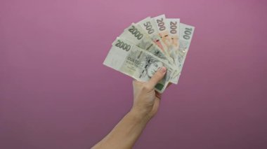 Kafkasyalı bir adam pembe duvarın karşısında Çech Koruna banknotları tutuyor. İzole edilmiş arka planda el ve para birimleri var..