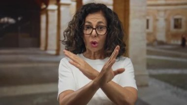 Orta yaşlı İspanyol kadın, eski şehir taş avlusunda inkar jesti olarak çıplak kollarını kavuşturuyor; reddediliyor..