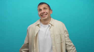 Gözleri kapalı beyaz bir adam yeşil bir duvarın önünde duruyor. Üzerinde bej bir tişört ve beyaz bir tişört olan tefekkür ifadesini sergiliyor..